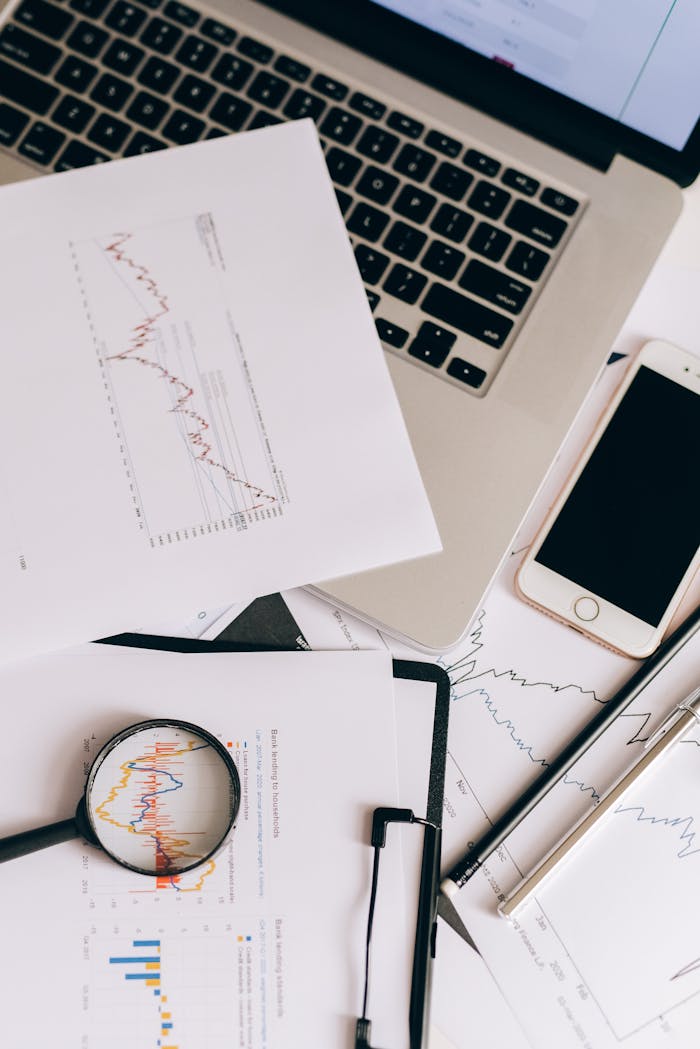 About Flat lay of office desk with graphs, laptop, smartphone, and magnifying glass for data analysis.